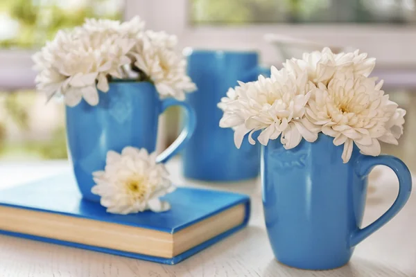 Schöne Blumen in Tassen auf einem Holztisch — Stockfoto