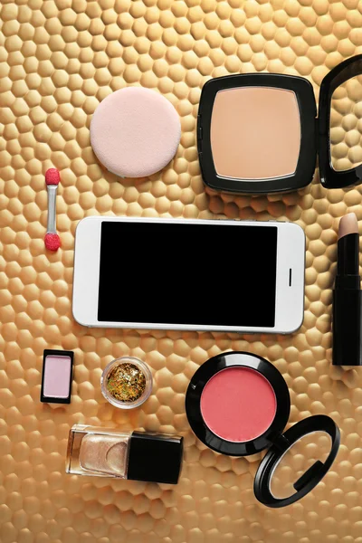 Cosméticos decorativos e smartphone em fundo dourado — Fotografia de Stock