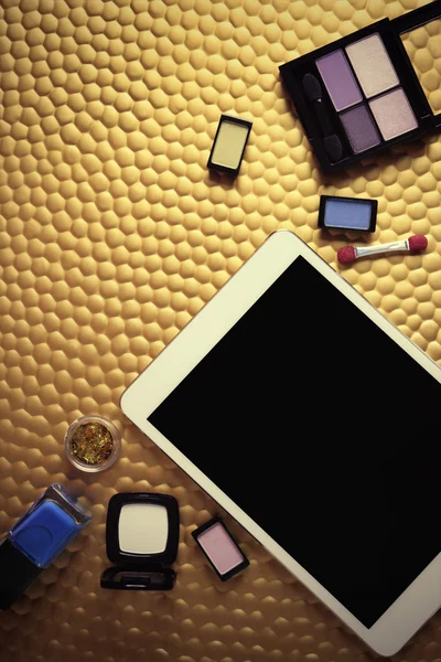 Cosméticos decorativos e tablet sobre fundo dourado — Fotografia de Stock