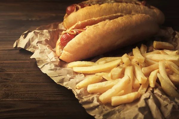 Saborosos cachorros-quentes e batatas fritas em fundo de madeira — Fotografia de Stock