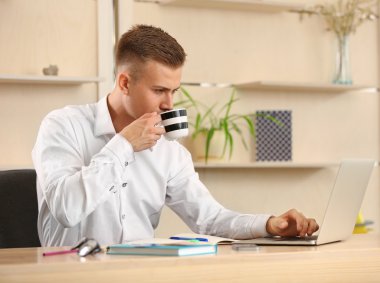 Dizüstü bilgisayarda çalışan ve ofiste kahve içme genç adam