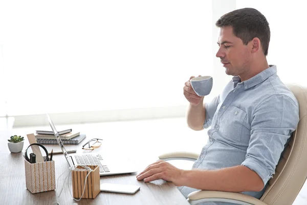 Hombre guapo trabajando en el ordenador portátil y beber café en la oficina — Foto de Stock