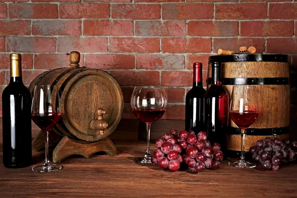 Vasos de vino tinto, uvas y barricas de madera sobre un fondo de pared de ladrillo — Foto de Stock