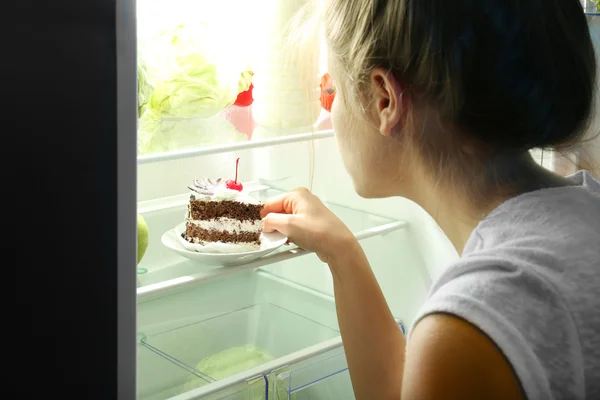 Girl taking cake from fridge. Unhealthy food concept