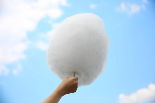 Female hand holding cotton candy on blue sky background — Stock Photo, Image