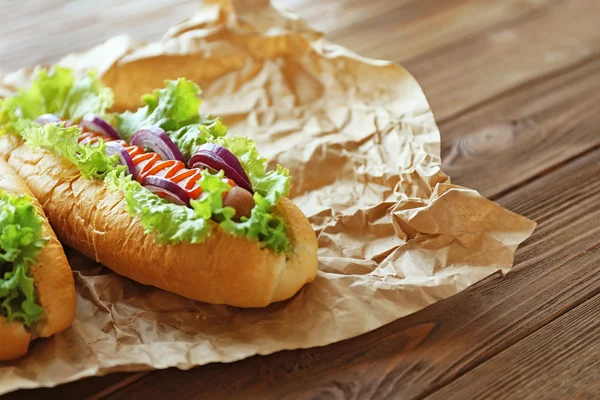 Gustosi hot dog su carta su sfondo di legno — Foto Stock