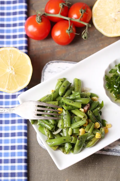 Salade met groene bonen en maïs en saus op plaat, op een houten achtergrond kleur — Stockfoto