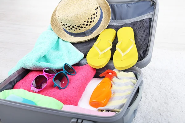 Maleta con cosas en alfombra blanca en el suelo para viajar a algún lugar cerca del agua para pasar las vacaciones de verano —  Fotos de Stock