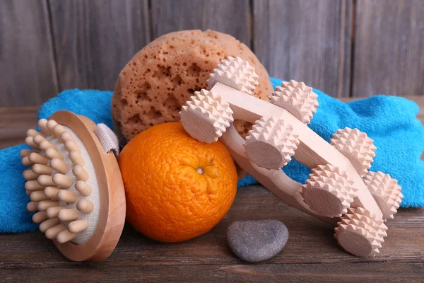 Roller brush, mop, towel, orange and oval brushes on wooden table in front of wooden wall — Stock Photo, Image