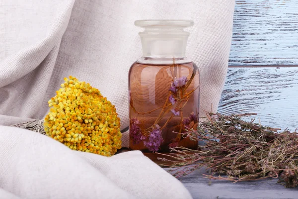 Bottles of herbal tincture and dried herbs on a napkin on wooden background in front of curtain — Stock Photo, Image