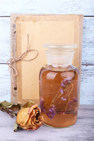 Bottles of herbal tincture, book and dried rose on wooden background — Stock Photo, Image