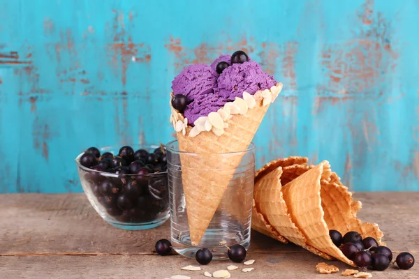 Tasty ice cream with berries in waffle cone on blue wooden background — Stock Photo, Image