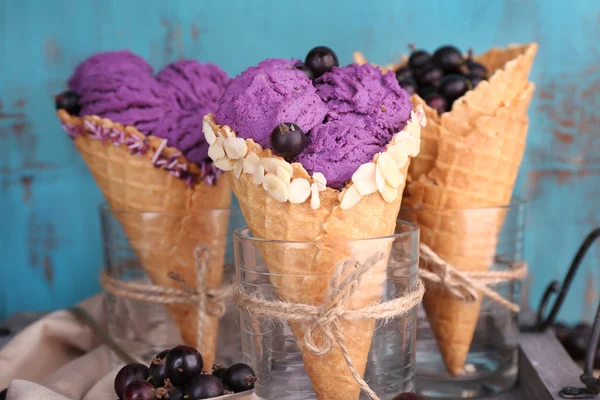 Gustoso gelato con bacche in coni di cialde su sfondo blu in legno — Foto Stock