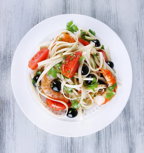 Gamberi freschi con spaghetti, olive, pomodori e prezzemolo in un grande piatto rotondo su fondo di legno — Foto Stock