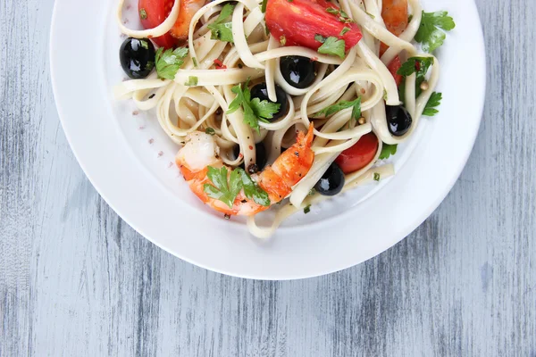 Fresh prawns with spaghetti, olives, tomatoes and parsley in a big round plate on wooden background — Stock Photo, Image