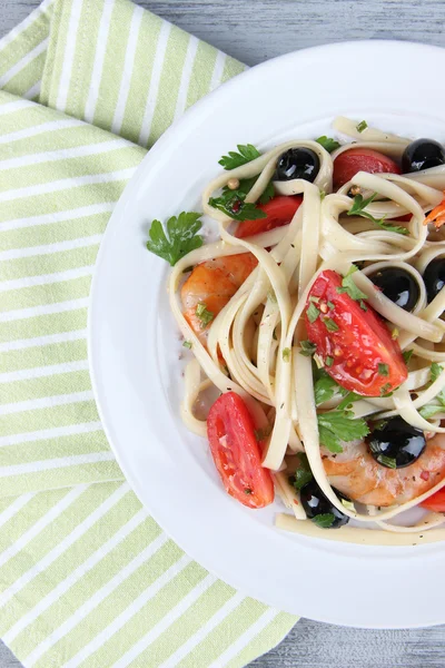 Fresh prawns with spaghetti, olives, tomatoes and parsley in a big round plate on napkin on wooden background — Stock Photo, Image