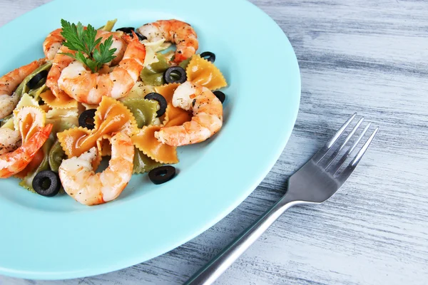 Fresh prawns with coloured macaroni, olives and parsley in a big blue round plate with a fork on wooden background — Stock Photo, Image