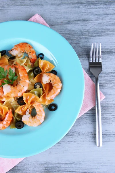 Fresh prawns with coloured macaroni, olives and parsley in a big blue round plate with a fork on wooden background — Stock Photo, Image