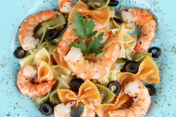 Fresh prawns with coloured macaroni and olives in a blue plate closeup — Stock Photo, Image