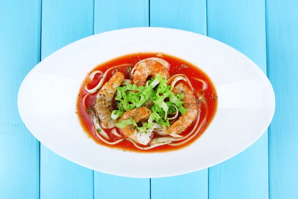 Crevettes fraîches avec spaghettis et laitue en sauce tomate dans un bol ovale blanc sur fond de bois bleu — Photo