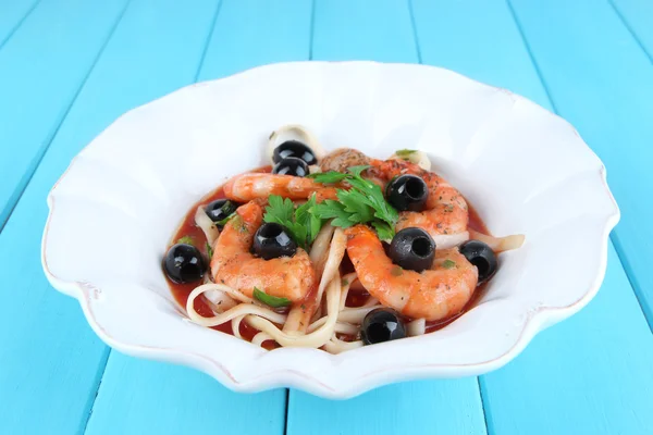 Fresh prawns with spaghetti, olives and parsley in tomato sauce in a round white plate on blue wooden background — Stock Photo, Image