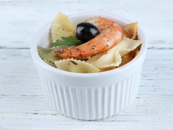 Fresh prawns with coloured macaroni and olives in a round bowl on wooden background — Stock Photo, Image