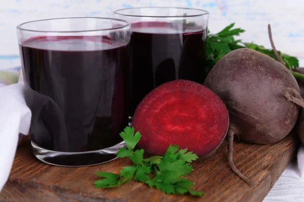 Copos de suco de beterraba fresca e legumes na tábua de corte em fundo de madeira — Fotografia de Stock