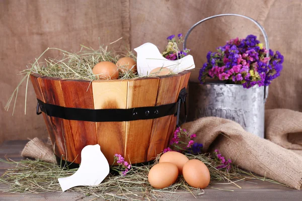 Big round basket with dried grass and fresh eggs on sacking background — Stock Photo, Image