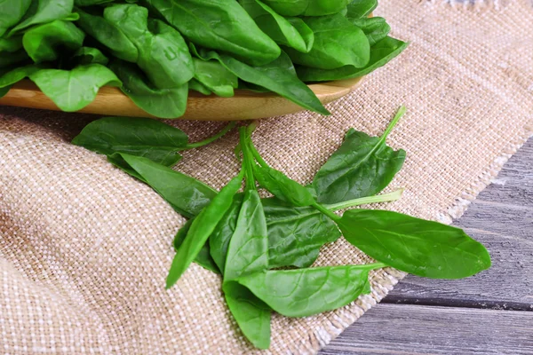 Tuft of fresh sorrel in wooden plate on piece of sacking on wooden background — Stock Photo, Image