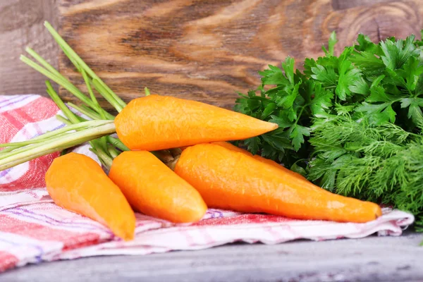 Carrots, dill and parsley on napkin on cutting board on wooden background — Stock Photo, Image