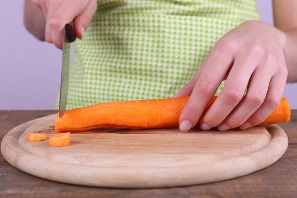 Frau schneidet Karotte mit Messer in Küche auf hellem Hintergrund — Stockfoto