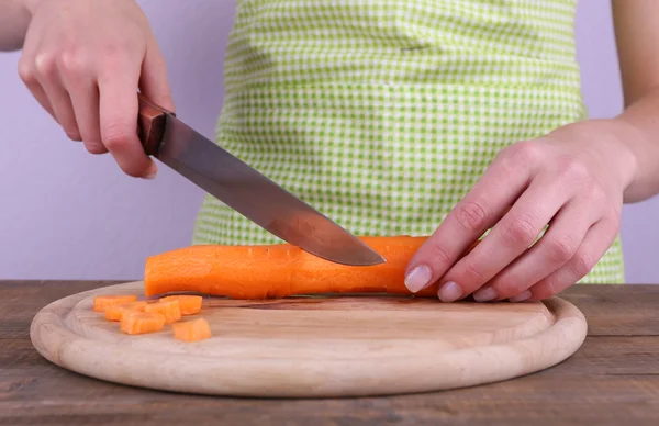 Woman cutting carrot with knife in kitchen on light background — Stock Photo, Image