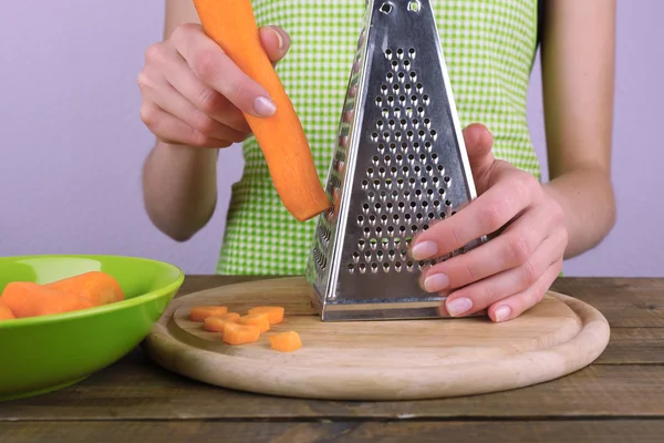 Woman grating carrot in kitchen on light background — Stock Photo, Image