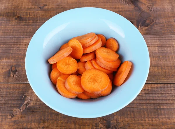 Slices of carrot in blue round bowl on wooden background — Stock Photo, Image