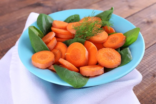 Slices of carrot, sorrel and dill in blue round bowl on napkin on wooden background — Stock Photo, Image