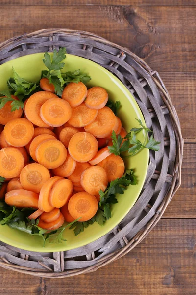 Fette di carota, acetosa e prezzemolo in ciotola rotonda verde su vimini incontrati su fondo di legno — Foto Stock
