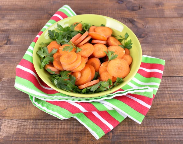 Slices of carrot, sorrel and parsley in green round bowl on napkin on wooden background — Stock Photo, Image