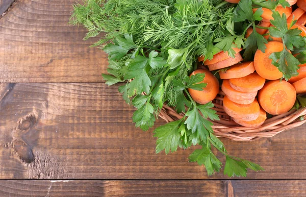 Slices of carrot and parsley in wicker bowl on wooden background — Stock Photo, Image