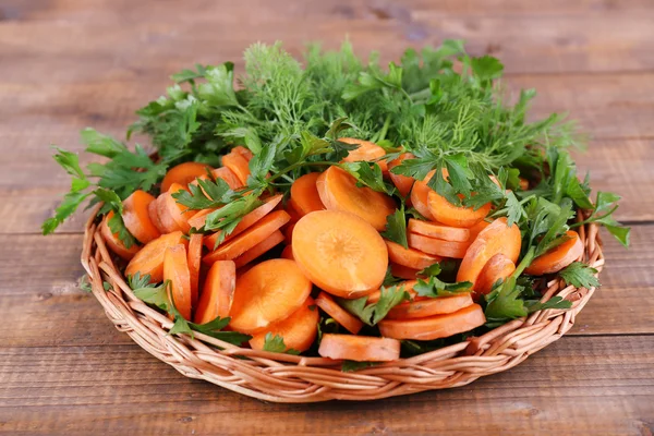 Slices of carrot and parsley in wicker bowl on wooden background — Stock Photo, Image