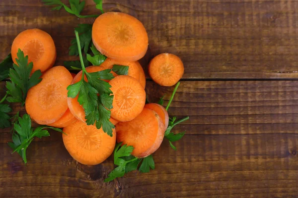 Slices of carrot and parsley on wooden background — Stock Photo, Image