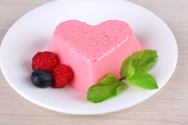 Pastel en forma de corazón con bayas en plato sobre fondo de madera —  Fotos de Stock