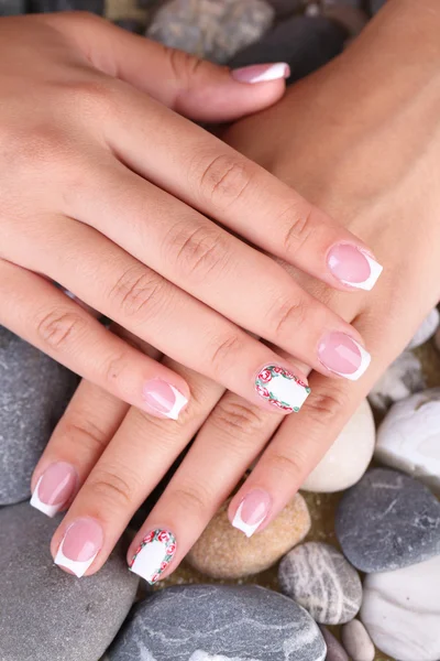 Female hand with stylish colorful nails on sea pebble background — Stock Photo, Image