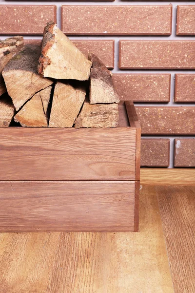 Wooden box of firewood on floor on brick background — Stock Photo, Image