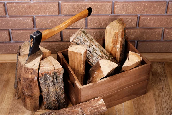 Box of firewood and axe on floor on brick background — Stock Photo, Image