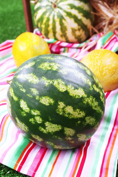 Melons and watermelons on napkin in wooden box on green background — Stock Photo, Image