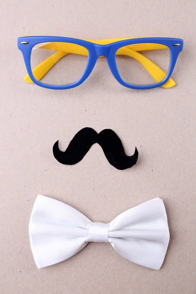 Glasses, mustache and bow tie forming man face on color background — Stock Photo, Image