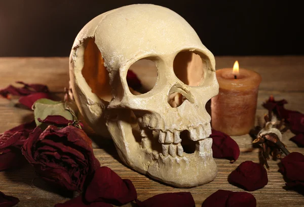 Crânio humano com pétalas de rosa secas e vela na mesa de madeira, close-up — Fotografia de Stock