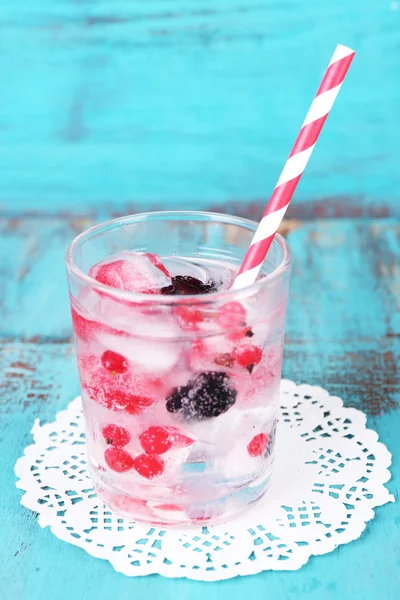 Cold cocktail with forest berries, frozen in ice cubes on color wooden background — Stock Photo, Image