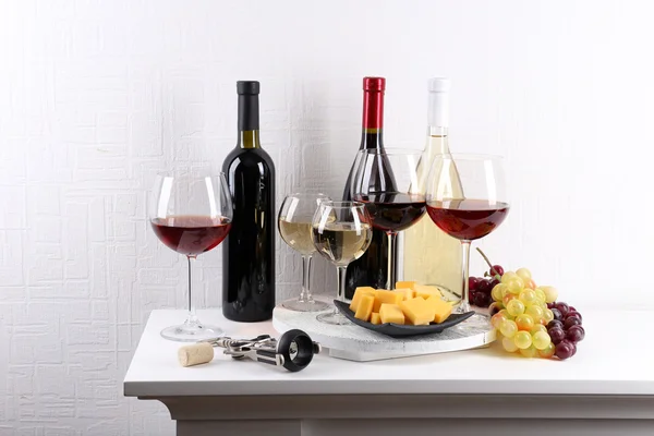 Bottles and glasses of wine, cheese and ripe grapes on table in room — Stock Photo, Image