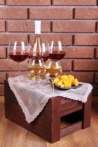 Bottle and glasses of wine and cheese on table on brick wall background — Stock Photo, Image